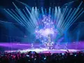 Wokalistka na scenie Eurowizji, otoczona tancerzami i efektami świetlnymi. Widownia filmuje występ, zastanawiając się, ile krajów w finale Eurowizji.