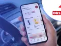 Dłoń trzyma smartfon z aplikacją ORLEN Pay, pokazującą punkty VITAY i nagrody. Kierownica samochodu w tle.