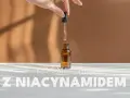 Dłoń trzyma pipetę z serum, nad buteleczką z brązowego szkła. Kosmetyki z niacynamidem to sekret pięknej skóry.