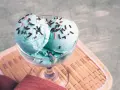 Ein Glas mit blauem Smurf-Eis, bestreut mit bunten Streuseln, steht auf einem Holzuntersetzer.