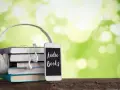 Słuchawki, stos książek i telefon z napisem "Audio Books" – idealne połączenie do odkrywania najpiękniejszych słuchowisk dla dzieci.