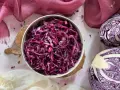 Insalata di cavolo cappuccio rosso, condita con petali di fiori, accanto a un cavolo cappuccio rosso tagliato a metà.