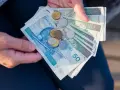Ręce trzymają polskie banknoty 50 i 100 zł oraz monety. To może być kwota na bon oświatowy.