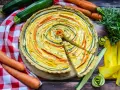 Eine bunte, vegetarische Quiche mit Zucchini und Karotten, kunstvoll im Kreis arrangiert. Frisch und lecker!