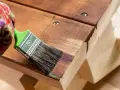 Mano guantata applica una tinta scura per dare un aspetto invecchiato al legno di una panca.