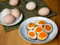 Na talerzu leżą połówki jajek do ramenu z płynnym, pomarańczowym żółtkiem. Obok całe jajka.