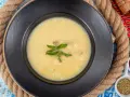 Un plato de sopa de pescado cremoso y caliente, decorado con hojas verdes, sobre un fondo rústico.