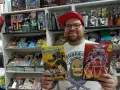 Mann mit Brille und roter Kappe hält zwei Comics in einem Comicladen.