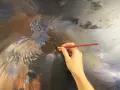 Une main tient un pinceau rouge, ajoutant des touches de lumière à une peinture à l'huile complexe d'un ange. La peinture à l'huile, c'est bien difficile, mais le résultat est saisissant.