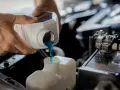 Hands pour blue coolant into a car's reservoir. This maintenance task is essential for preventing overheating, which can lead to costly car radiator replacement.