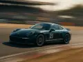 Une Porsche 911 noire, numéro 21, file sur un circuit. Le mouvement est capturé par un photo filé, créant un flou artistique autour de la voiture.