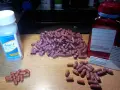 Kapsułki Asacol i inne leki na drewnianym blacie. Wiele różowych kapsułek leży obok butelki Asacol.