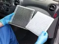 A dirty cabin air filter can make your car smell. A gloved hand holds a very dirty filter next to a clean, white one, showing the stark contrast.