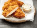 Délicieux poulet pané croustillant, coupé en deux pour montrer sa tendreté, servi avec une sauce crémeuse.