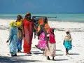 Kobiety w kolorowych strojach spacerują po plaży. Czy Zanzibar to państwo? Tak, to autonomiczny region Tanzanii, znany z pięknych plaż.