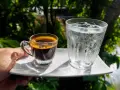 Espresso i szklanka wody z lodem na białym talerzyku. Woda do espresso przed czy po?