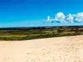 En person i röd jacka vandrar på en sanddyn vid Jyllands strand. Landskapet sträcker sig mot en blå himmel med vita moln.