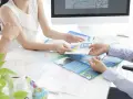 Ludzie przeglądający mapy i broszury podróżne przy biurku z komputerem.