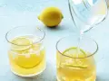 Erfrischendes zitronenwasser am morgen wird in ein Glas mit Eis und Zitronenscheiben gegossen. Eine ganze Zitrone liegt daneben.