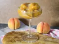 Erfrischendes Pfirsich-Prosecco-Sorbet in einem eleganten Glas, daneben reife Pfirsiche.