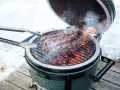 Un succulento bistec a la fiorentina cuoce sulla griglia di un Big Green Egg, circondato da fumo e fiamme.