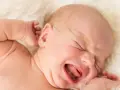 Płacz dziecka podczas 4 skoku rozwojowego. Maluch wyciąga rączki, zamyka oczy, a jego buzia jest otwarta w głośnym krzyku.