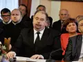Jarosław Paluch w czarnym garniturze siedzi przy stole, otoczony innymi osobami.