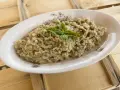 Hummus di melanzane cremoso, guarnito con basilico fresco, servito in un piatto ovale su un tavolo di legno grezzo.