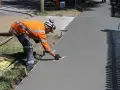 Robotnik w pomarańczowej kamizelce wygładza świeży beton kielnią.