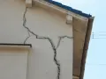 Duże pęknięcia na białej ścianie domu świadczą o osiadaniu gruntu.