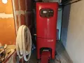 Chaudière rouge Chappée dans une pièce. Un tuyau blanc enroulé est accroché au mur. Pensez à l'assurance chaudière pour votre confort.