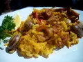 Arroz con conejo, un plato tradicional con trozos de carne dorada, arroz amarillo y caracoles, adornado con perejil y limón.