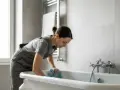 Donna in tuta pulisce la vasca da bagno smaltata con un panno blu, mostrando come sbiancare vasca da bagno smaltata.