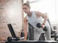 Kvinna tränar med hantlar på gym, fokuserad på att bygga muskler och gå upp i vikt.