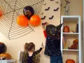 Dzieci tworzą **dekoracje halloween diy**: wieszają nietoperze na ścianie, obok pajęczyny i balonów.