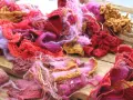 En hög av garn och stickade tygbitar i rosa, rött och lila. En del har en fin stickad kant som inte rullar sig.