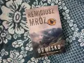 Okładka najnowszej książki Remigiusza Mroza "Urwisko". Góry, mgła i samotna postać na szczycie.