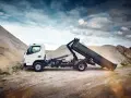 Biały Mitsubishi Canter z podniesioną skrzynią ładunkową na tle żwirowych hałd.