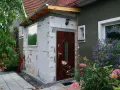 Trwa rozbudowa budynku gospodarczego. Nowa część z białych pustaków, brązowe drzwi, okno i zielone rośliny.