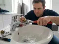 Plombier répare un robinet qui fuit dans une salle de bain. L'eau coule dans le lavabo pendant qu'il utilise une clé.