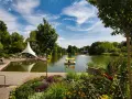 Ein sonniger Tag am Badesee Mannheim. Mehrere Tretboote mit gelben Verdecken gleiten über das Wasser, umgeben von üppigem Grün und blühenden Blumen.