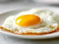 Un œuf au plat parfait, cuit à la perfection dans l'air fryer, avec un jaune d'or éclatant sur un lit de blanc d'œuf aérien.