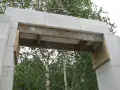 Konstrukcja nadproża z bloczków betonowych, podparta drewnianymi belkami, w otoczeniu drzew.