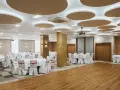 Elegancka sala bankietowa gotowa na wesele we wrześniu. Okrągłe stoły z białymi pokrowcami i czerwonymi wstążkami czekają na gości.