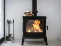 Estufa de leña con fuego vivo, lista para canalizar aire y chimenea. A su lado, un atizador y escoba.