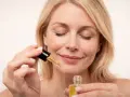 Kobieta z zamkniętymi oczami aplikuje serum z **retinolem**, dbając o skórę, by uniknąć efektów **solarium**.