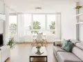 Un luminoso salón estilo nórdico con sofá gris, mesa de centro de madera y grandes ventanales con vistas a palmeras.