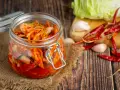 Słoik z kimchi na tle desek, z kapustą, czosnkiem i papryczkami chili.