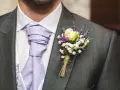 Elegancki pan młody z fioletowym krawatem i bukiecikiem kwiatów do butonierki, ozdobionym lawendą i białymi drobinkami.