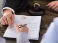 Gerichtlicher Hammer und Eheringe auf Scheidungsdokumenten. Ein Anwalt zeigt auf einen Paragraphen, während eine Person unterschreibt. Ein wichtiger Termin, der vielleicht Sonderurlaub erfordert.